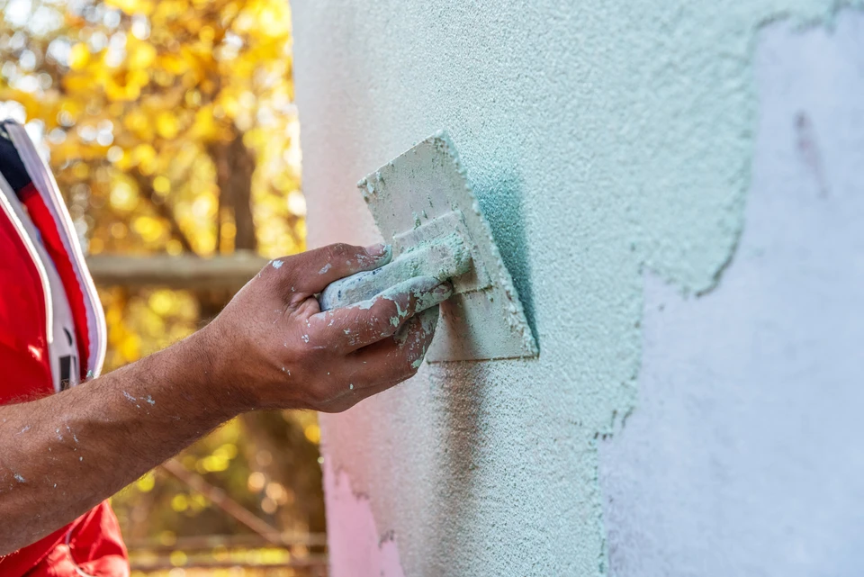 Ouvrier appliquant un enduit de façade sur mur extérieur avec taloche, travaillant en plein air sous lumière naturelle